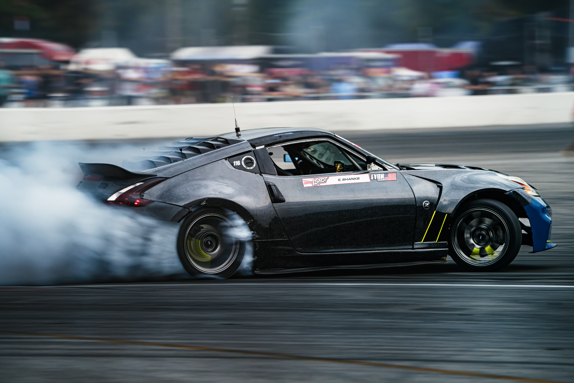 Black sports car performing a drift on a track with spectators in the background